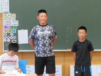 男の子2名が黒板の前に立ち、その横で座っている男の子が資料のようなものを見ている結団式での写真