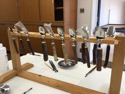 木製の台に柄の部分がそれぞれ違うスプーンが並べて吊るされている写真