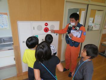 オレンジの服を着た消防隊員の人が子供4名に火災報知機の説明をしている写真