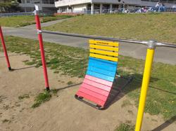 鉄棒の少し離れた所に黄色、青色、赤色の三色の少しカーブがある細長い逆上がり練習器が置かれた写真