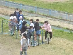 校庭に一輪車練習用の手すりの周りに一輪車に乗った児童が集まって練習をしている写真