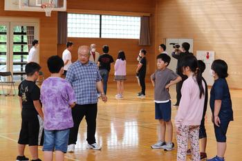 体育館内で講師の方と児童数名がひとつのグループになり、円になって立ち、説明を聞いている様子を写した写真