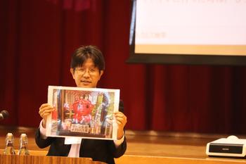 演台にたつ男性が大きな写真をみせながら話をしている写真