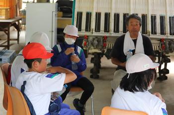 椅子に座りながら阿部さんの説明を聞いている体操服姿の児童4名の写真