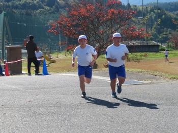 白い帽子を被った体操服の男子児童2名が並走しながらグラウンドの外を走っている写真