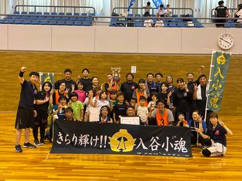 体育館で「きらり輝け！！入谷小魂」と書かれた黒い横断幕や「入小魂」ののぼり、賞状はトロフィーを持った大勢の大会参加者が集まって写した集合写真
