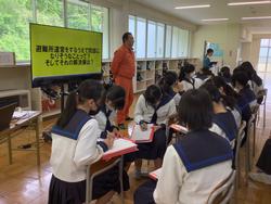 問題定義のかかれたモニター横に南三陸消防署の講師の男性が立ち、椅子に座っている生徒の皆さんがメモを取りながら話を聞いている消防署講話 の様子の写真