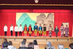 背景には山や岩を描いた大きな舞台セットがあり、子どもたちは舞台上に横一列に並びそれぞれが異なる衣装を着て舞台発表をしている写真