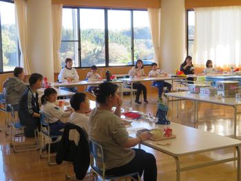 コの字に並べられた机に親子が並んで座り給食を楽しんでいる写真