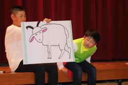 子どもがヤギの絵を描いた大きな紙を持ち、もう一人の子どもがそれをのぞき込んでいる様子の写真