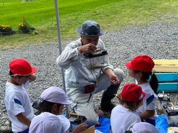 児童の前で農家の男性が虫の入ったかごを持ちながめている様子を写した写真