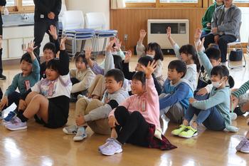 床に座った子供達数名が元気よく左手を上げている様子を写した写真