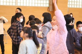 体育館に集まった大勢の子どもたちの中で、ピンクの服を着た女の子が右手を大きく上にあげている写真