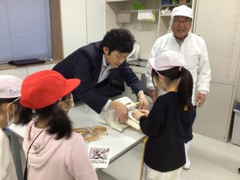 工場の係の人に包装袋に入ったかまぼこをお土産にもらうために並んでいる子供たちの写真