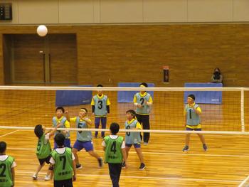 奥が水色のビブス、手前が緑色のビブスの男子チームが試合を行いボールが手前のチームにはいろうとしているミニバレーボール大会の写真