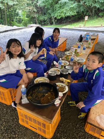 コンテナで机と椅子を作り、そこに座りながら食事を楽しんでいる4名の女の子と1名の男の子の写真