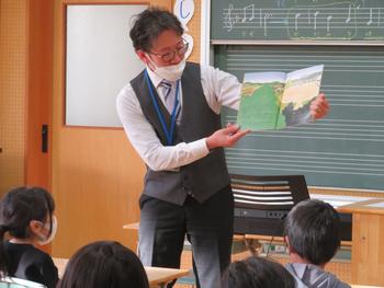 男性教諭が本を開きながら子供たちに読み聞かせをしている写真