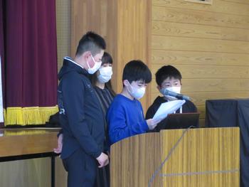 男の子3名が演台のマイクの前に並び、女性が見守る中青い服を着た男の子が発表をしている写真