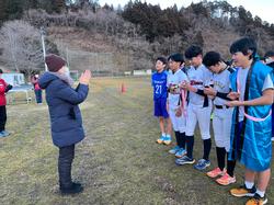 野球のユニフォームや水色の法被などを着た5人の男子生徒が横一列に並び、向かい合って立った人物が拍手を送っている様子の写真