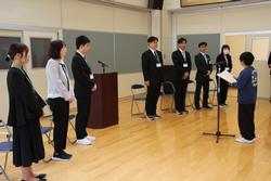 7名の先生の前に立ち歓迎のあいさつをしている男子生徒の写真