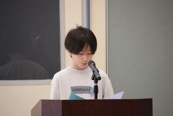 演題のマイクの前で代表児童が新年度の抱負を発表している写真