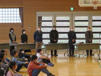 体育館の端に長机を設置し、講師の先生や学校運営協議会委員の皆様が立って挨拶をしている写真