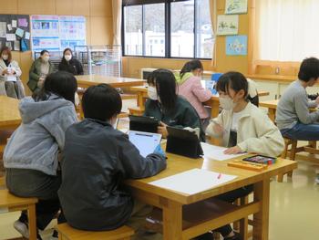 4人1組で机に座り授業をうけている子供達と教室の奥で授業を見学している保護者の方の写真