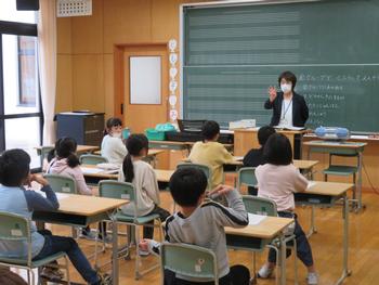 女性教諭が指を使いながら子供たちに教えている授業の様子を写した写真