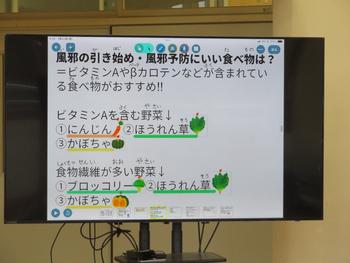 風邪の引き始めや予防に効果的な食べ物として、ビタミンAやβカロテンを含むにんじん・ほうれん草・かぼちゃ、食物繊維が豊富なブロッコリー・ほうれん草・かぼちゃが紹介されている風邪予防のための食べ物の説明が書かれた紙がモニターに掲示されている写真