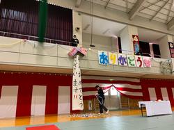 紅白幕で飾られた体育館の2階から下げられたくす玉に「卒業おめでとうございます！！」と書かれた垂れ幕が下がり、壁には「ありがとう」と書かれた飾り付けがされている写真