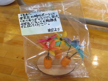 オレンジ色の繭を台座に花を飾った可愛らしい手作りの贈り物が、透明な袋にメッセージカードと一緒に入っている様子の写真