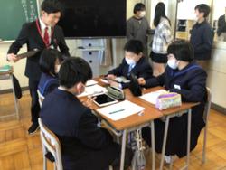 4人グループに分かれて活動をしている生徒たちの様子をスーツを着た男性が確認している授業参観の様子の写真