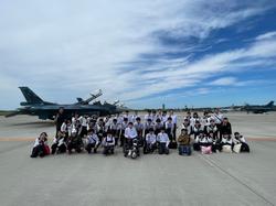 飛行場の滑走路上で戦闘機を背景に、多くの学生が制服姿で並び記念撮影をしている写真