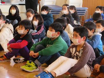 児童たちが同じ方向を向いて床に座り、熱心に話に耳を傾けている様子の写真