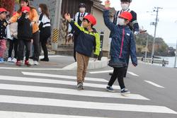警察官の方が見守る中、2人児童が手を挙げながら横断歩道を渡っている写真