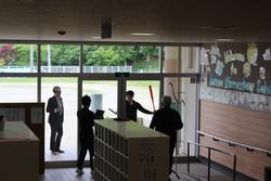 昇降口で、先生たちが刺股を使って不審者対応の訓練を行っている様子の写真