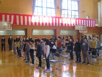 体育館で、多数の小学生と先生方が、式典のために整列して立っている様子を捉えた写真