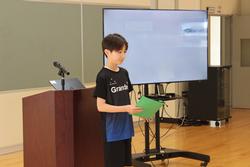 緑色の紙を持った男子生徒が演台を背にして立ち、プール学習の目標を発表している写真