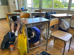 教室で生徒たちが机の下にもぐり頭を抱え、安全を確保している避難訓練の様子の写真