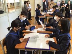 教室で生徒たちが4人グループに分かれて座り、並べた机にホワイトボードや資料を広げて活動に取り組み、後方で保護者から保護者が見学している様子の写真