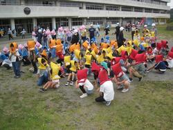 1次避難場所で子どもたちが色とりどりの防災頭巾をかぶって2列に並んでしゃがみ、次々と生徒たちが避難場所に集まってきている避難訓練をしている様子の南三陸町立入谷小学校の写真