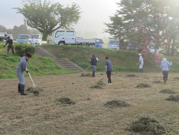 数名の人々が熊手を使って刈り取った雑草を集めている様子を写した奉仕作業の様子の写真