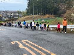 先生を先頭に生徒たちが一列に並び、道路のガードレール横を歩いている写真