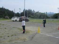運動場に車が2台駐車しており、職員の方が旗を持って誘導している様子の写真