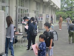 教室の裏口付近で、保護者が先生に迎えに来たことを伝え、子どもの引き渡しが行われている様子の写真