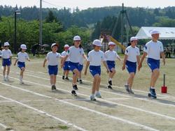 白い帽子をかぶった児童たちが隊列を組んで歩いている入場行進の写真