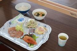 白いご飯、味噌汁、豚肉の生姜焼きやフライ、サラダ、ヨーグルトなどが並んだ和洋折衷の食事の写真