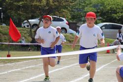 2人の男子児童が並ぶようにゴール直前まで走り込んでゴールテープを目指して全力で走っている写真