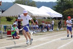 白い帽子をかぶった男子児童が勢いよくゴールテープを切っている瞬間が写されている写真