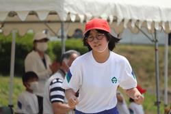 メガネをかけ赤い帽子をかぶった女子児童が必死に走っている様子を写した写真